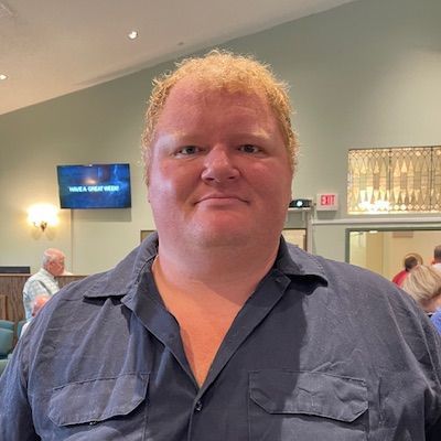 Smiling person in a blue shirt standing indoors at a reception area