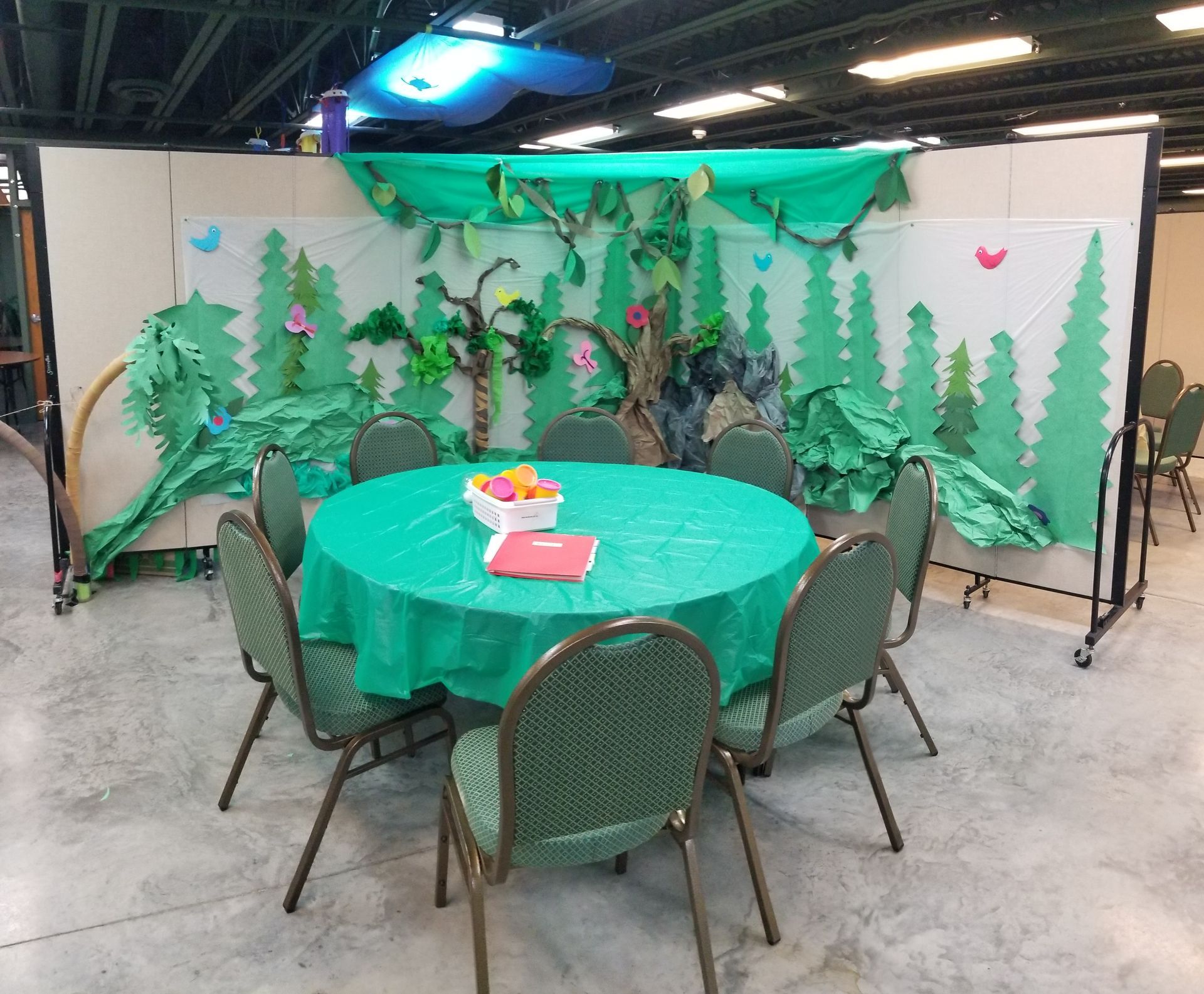 Round green table with chairs in front of a woodland-themed event backdrop