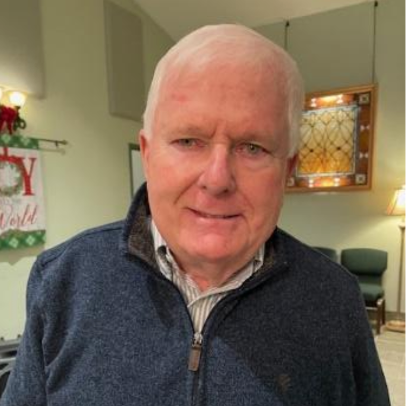 Smiling man in a blue sweater indoors, with a lamp and framed art in the background