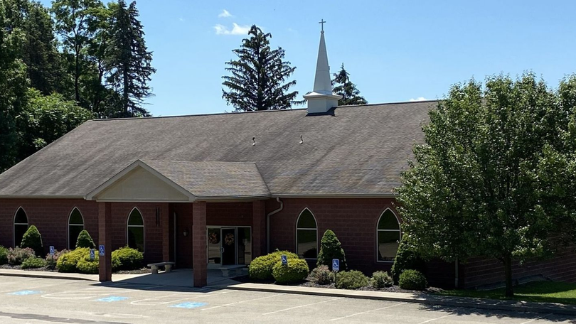 Brick building with a gray roof, white steeple, and trees in front under a clear sky