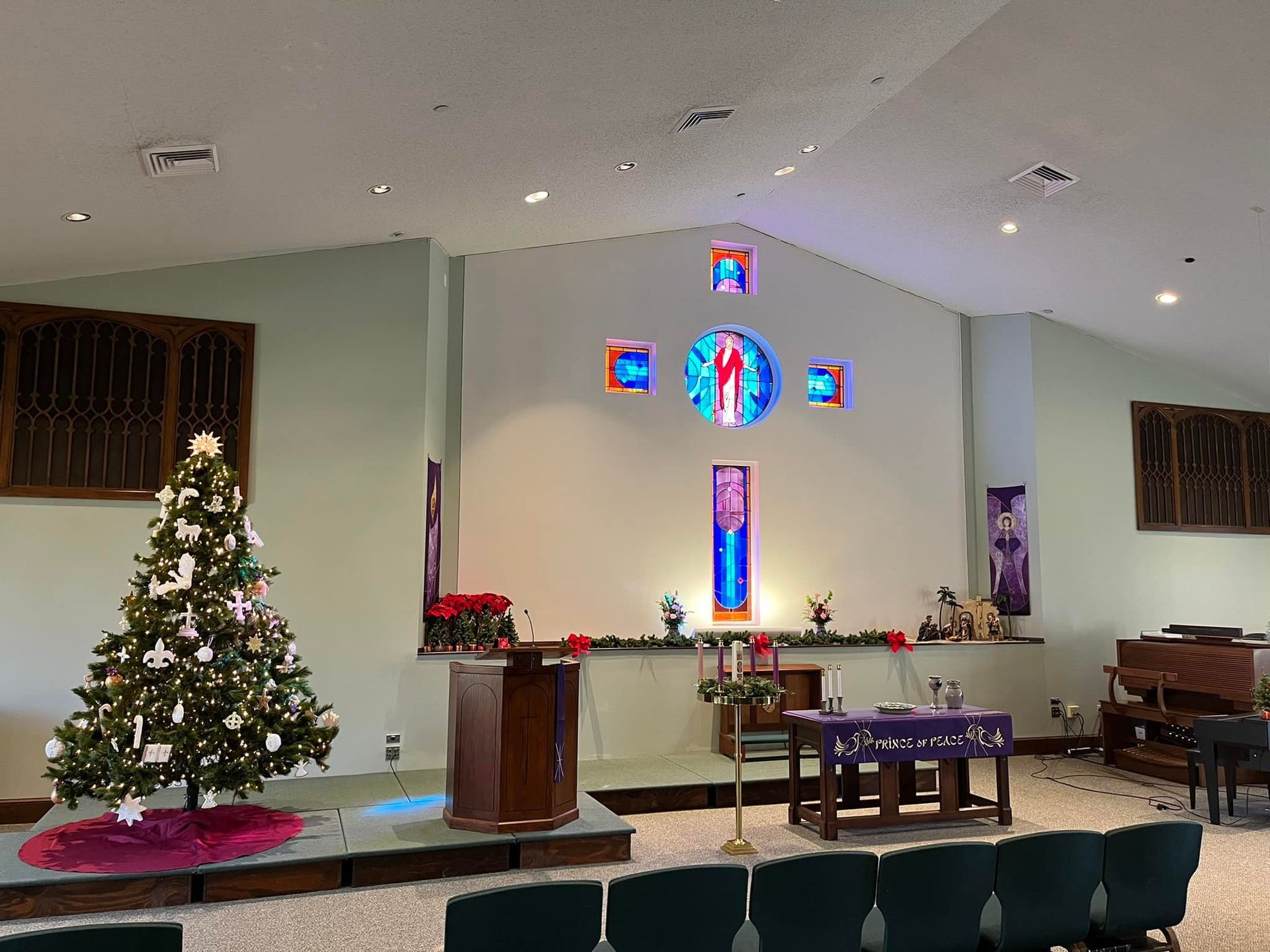 Decorated church altar with Christmas tree, stained-glass cross, candles, and purple Advent cloths