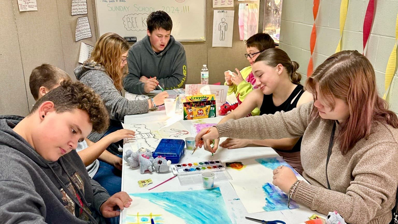 People gathered around a table, working on colorful art projects in a classroom-like setting
