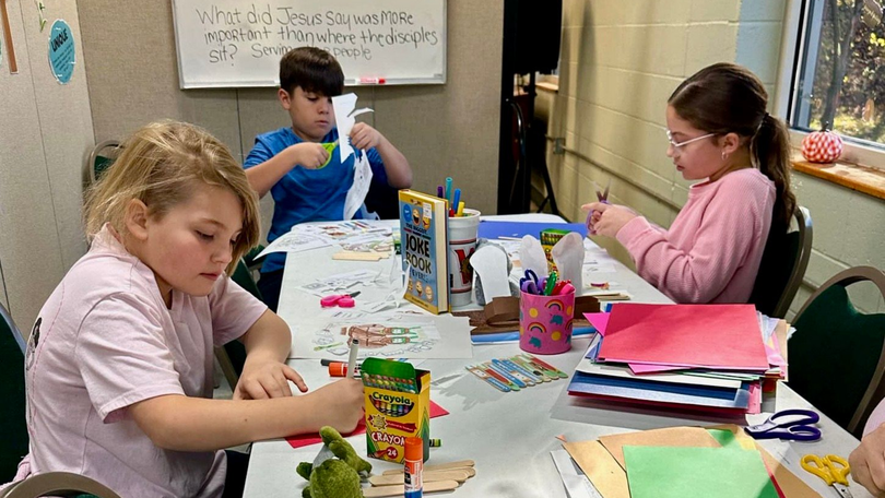 Children doing arts and crafts at a table with paper, markers, and supplies in a classroom