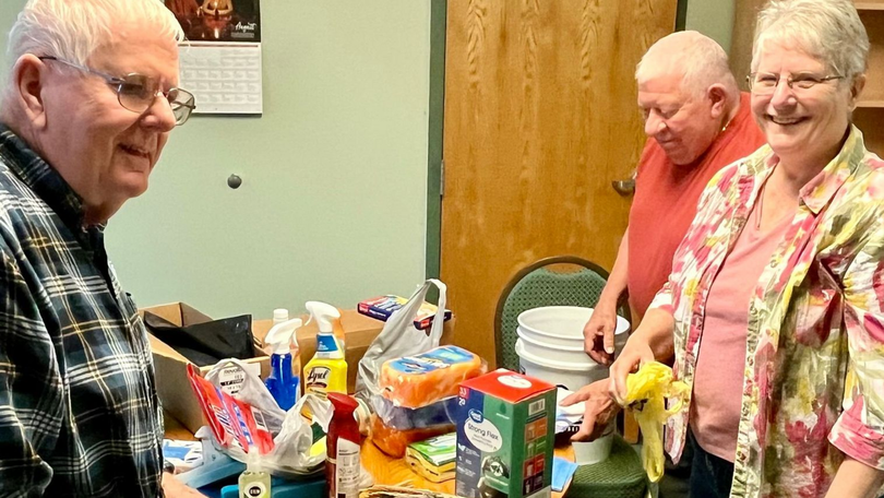 People standing by a table with assorted canned goods and packaged food in a community room