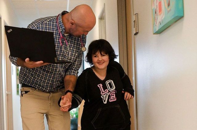 Two people smiling in a hallway, holding hands, with one carrying a laptop.