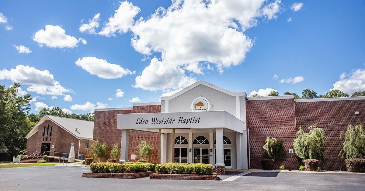 Exterior of the Cave Springs Baptist Church building on a sunny day with a blue sky and white clouds.