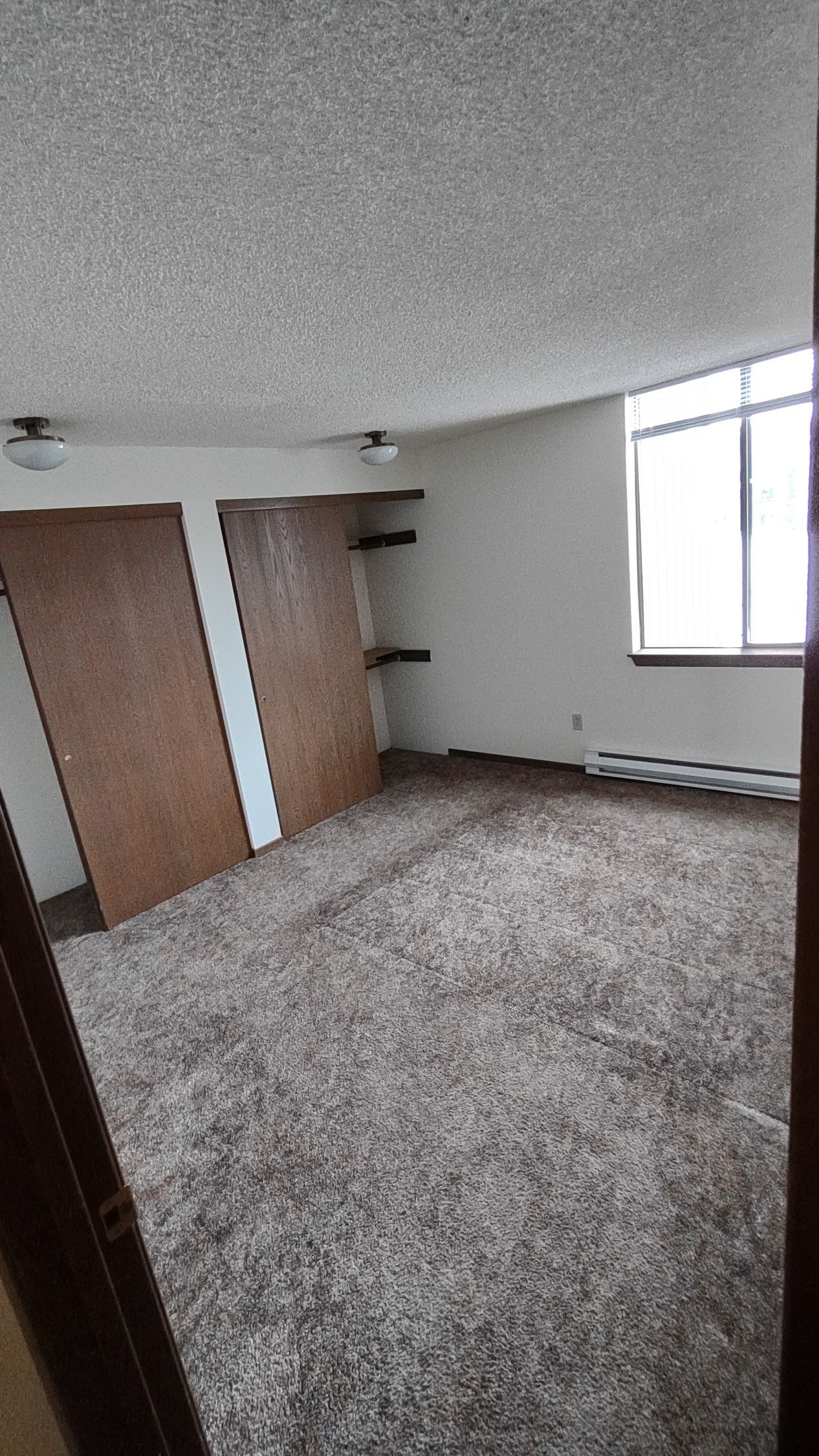 An empty living room with a carpeted floor and a window.