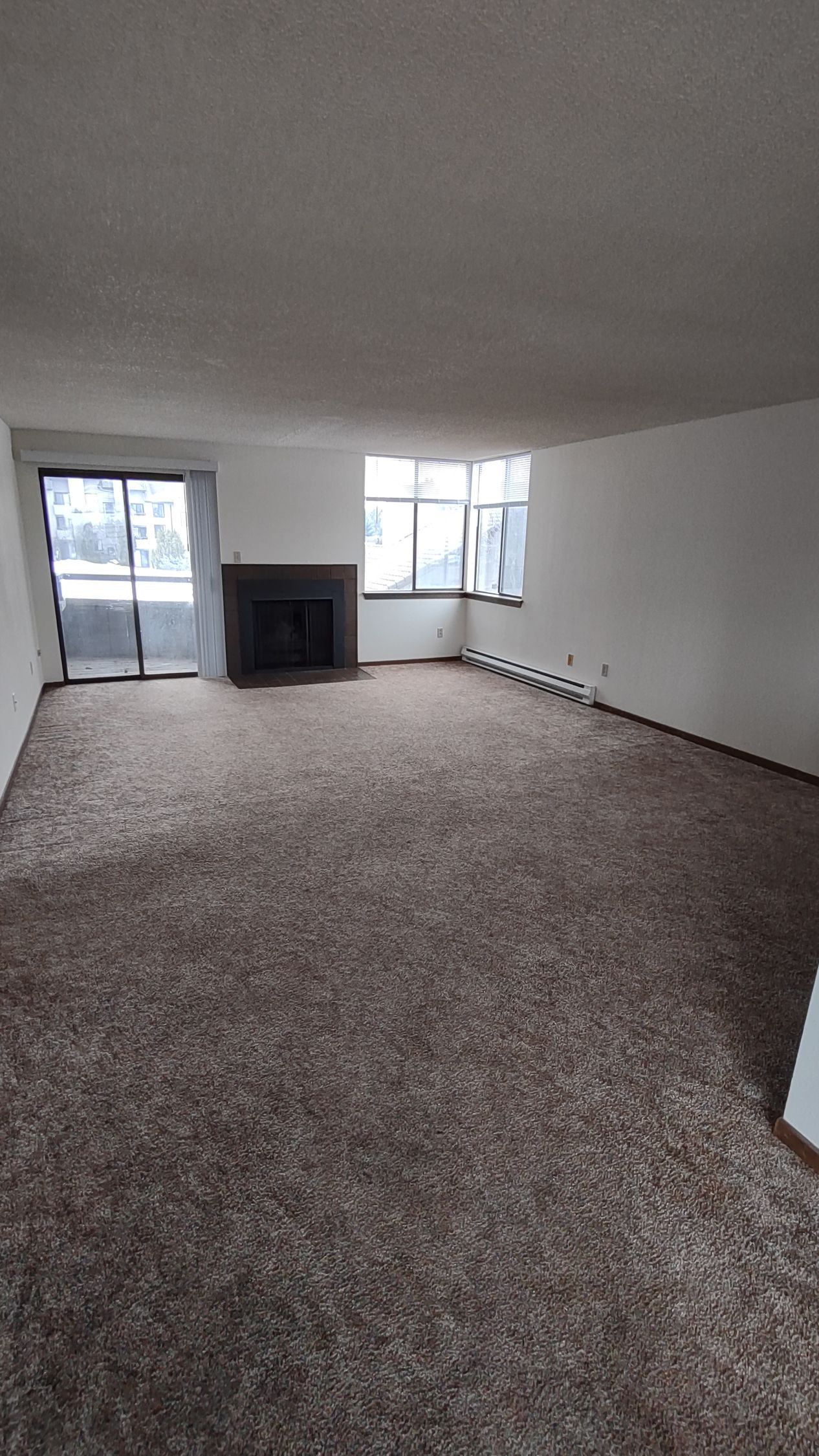 An empty living room with a fireplace and sliding glass doors.