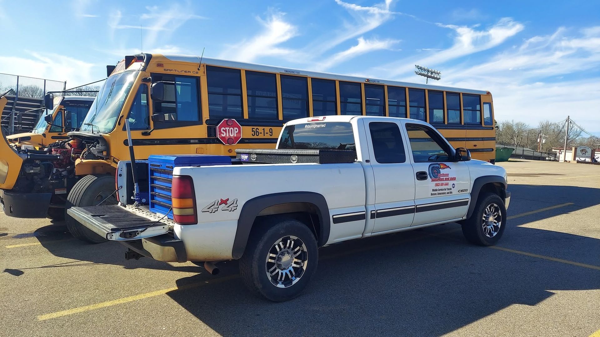 White pickup truck parked beside a yellow school bus on a sunny lot.