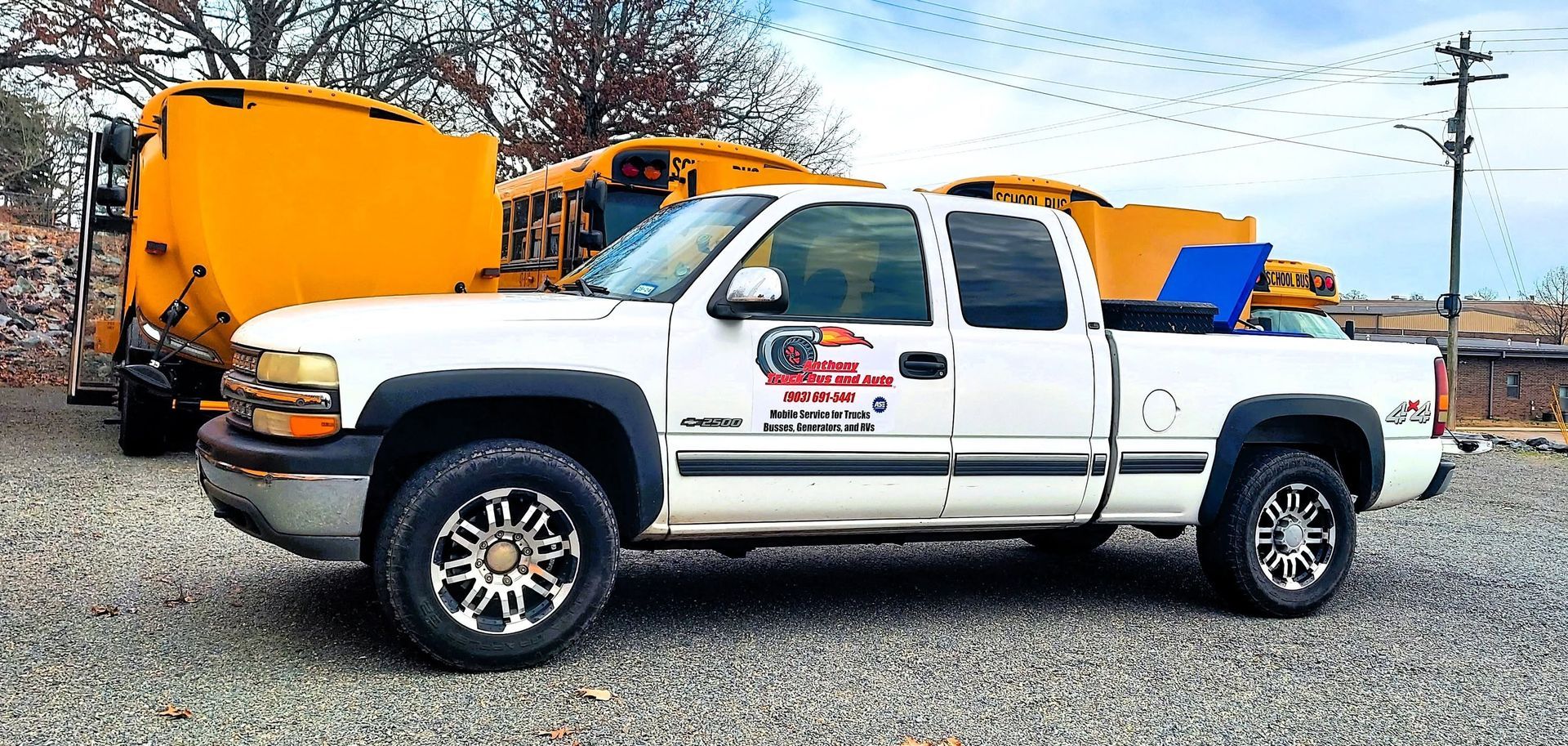 White utility pickup truck parked on gravel beside a yellow work truck and snowplow equipment