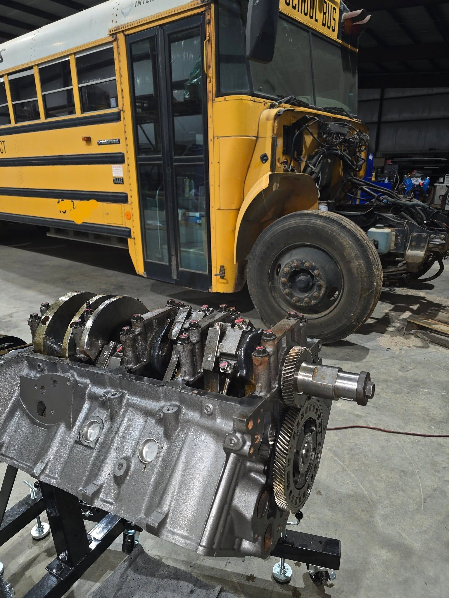 Damaged yellow school bus in a garage with a detached engine and front-end repair work