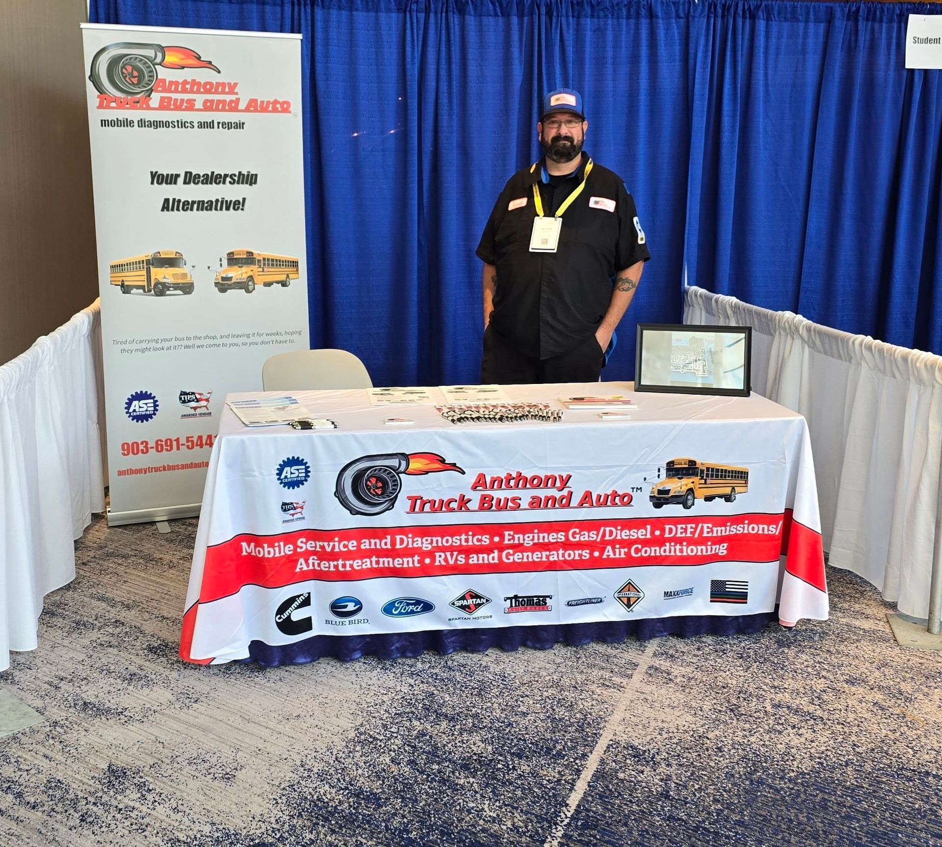 Trade show booth for Anthony Truck Bus Auto with banner, table, and a man standing behind the display.