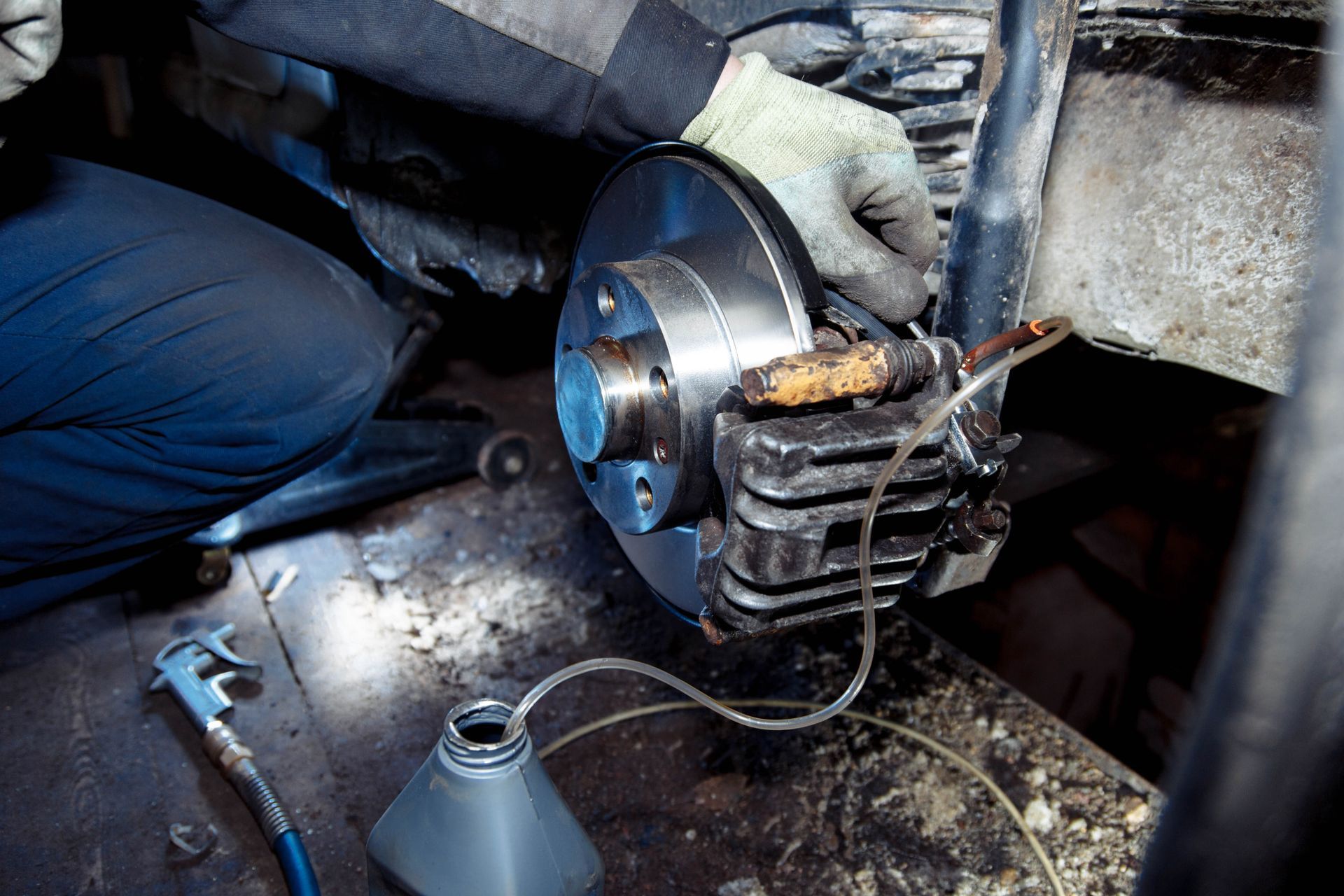 Mechanic replacing a car brake rotor with a wrench, wearing gloves in a workshop.