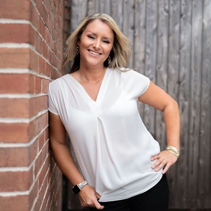 A woman in a white shirt is leaning against a brick wall.