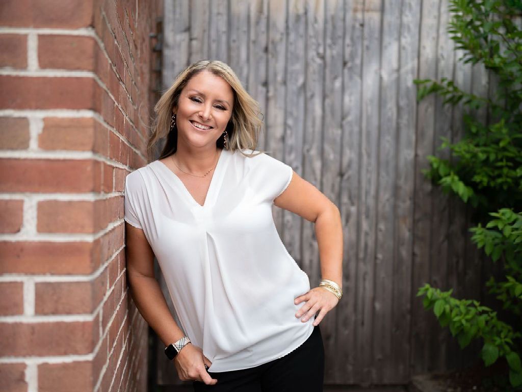 A woman in a white shirt is leaning against a brick wall.