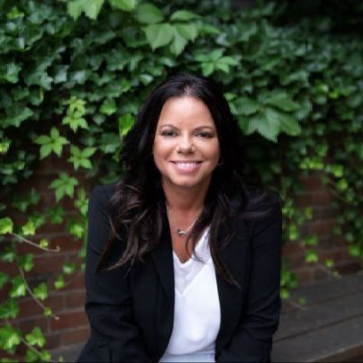 A woman in a black jacket and white shirt is sitting on a bench.