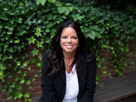 A woman in a black jacket and white shirt is sitting on a bench.
