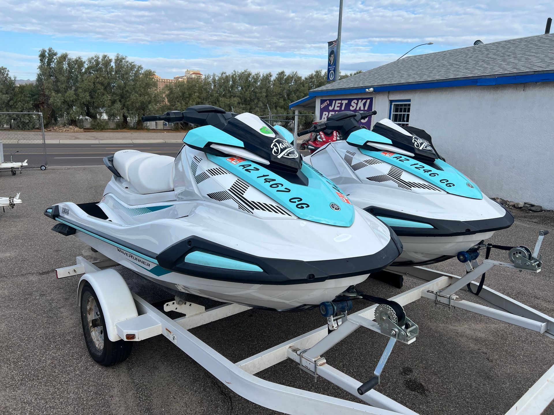 Two aqua and white jet skis on trailers parked outdoors near a building