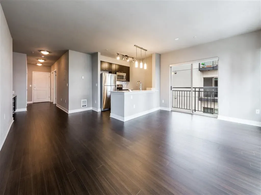 Spacious living room and kitchen area with dark wood floors and a balcony.