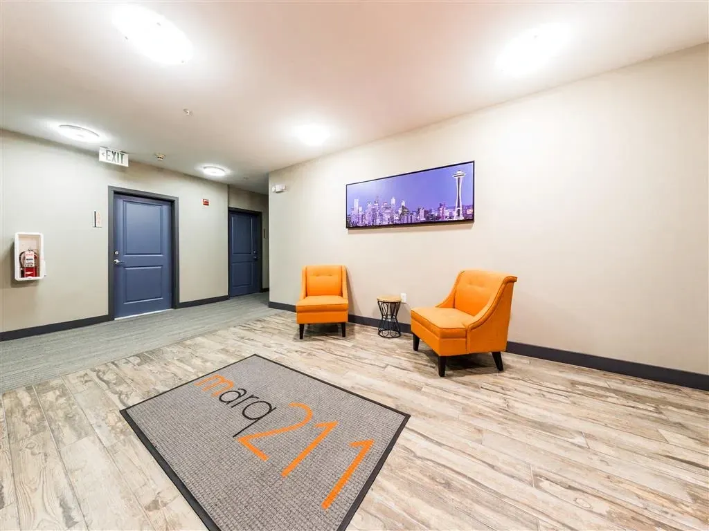 Hallway with two orange chairs, a side table, and artwork of a city skyline.