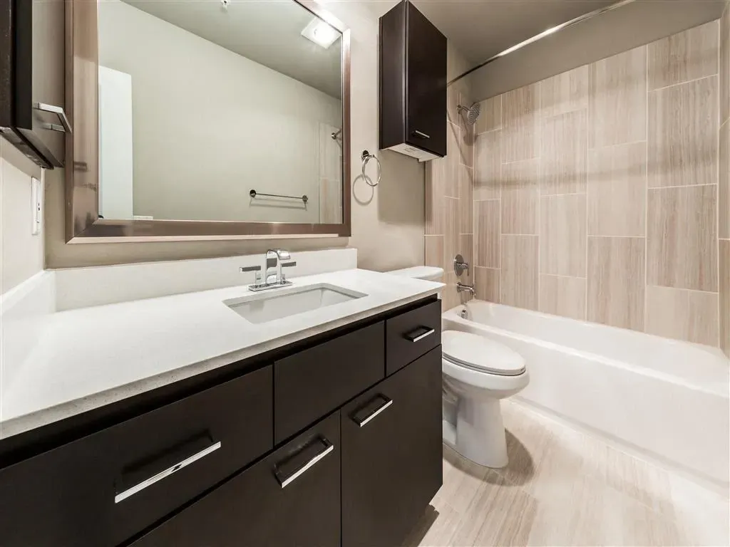 Bathroom with dark wood vanity, white countertop, large mirror, and tiled shower/tub area.