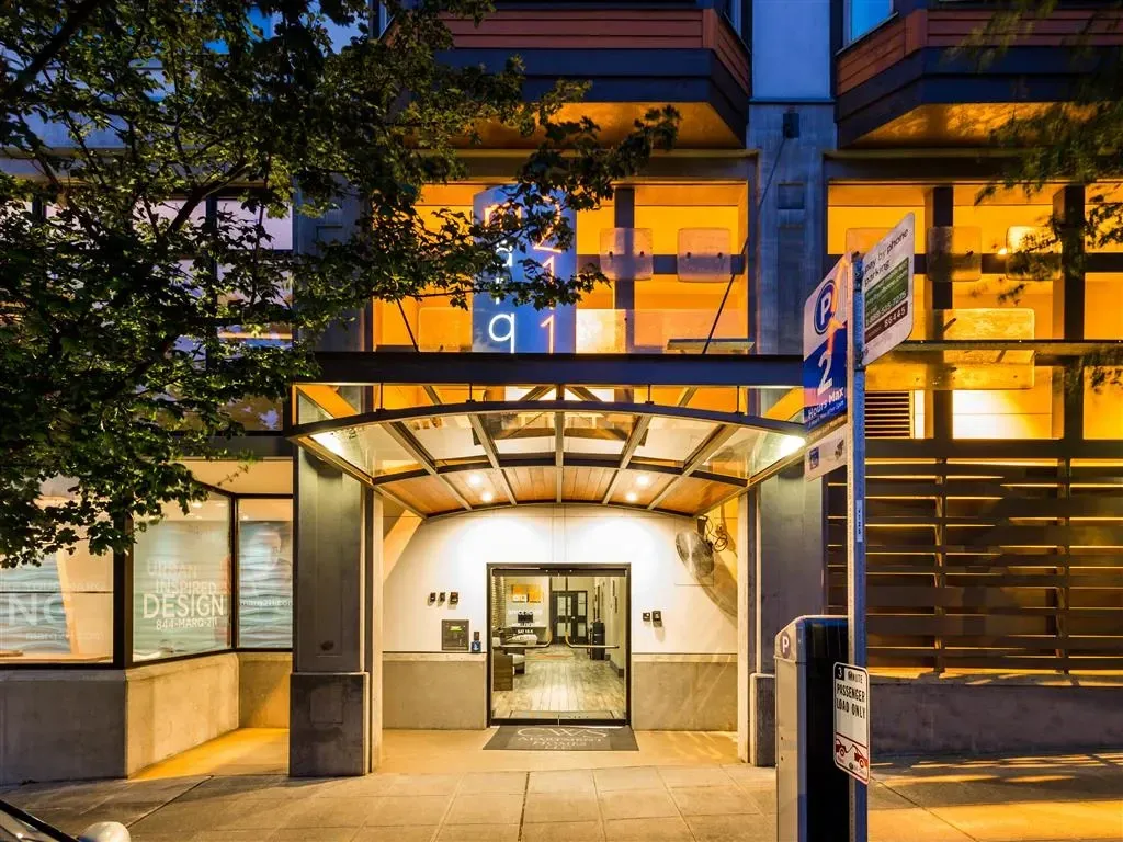 The entrance of the apartment building at night, with illuminated windows and signage.