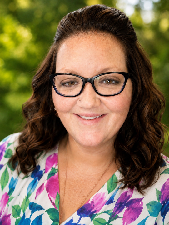 Smiling woman with glasses in a floral blouse against a blurred green background