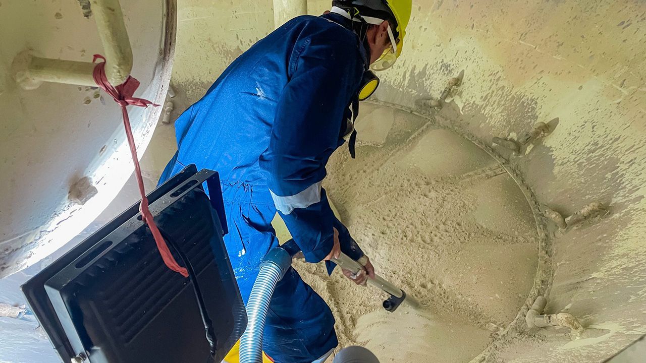 Un trabajador con traje protector azul inspecciona un techo dañado con aislamiento y material expuesto.
