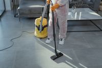 Person vacuuming a gray floor with a yellow vacuum in a modern living room