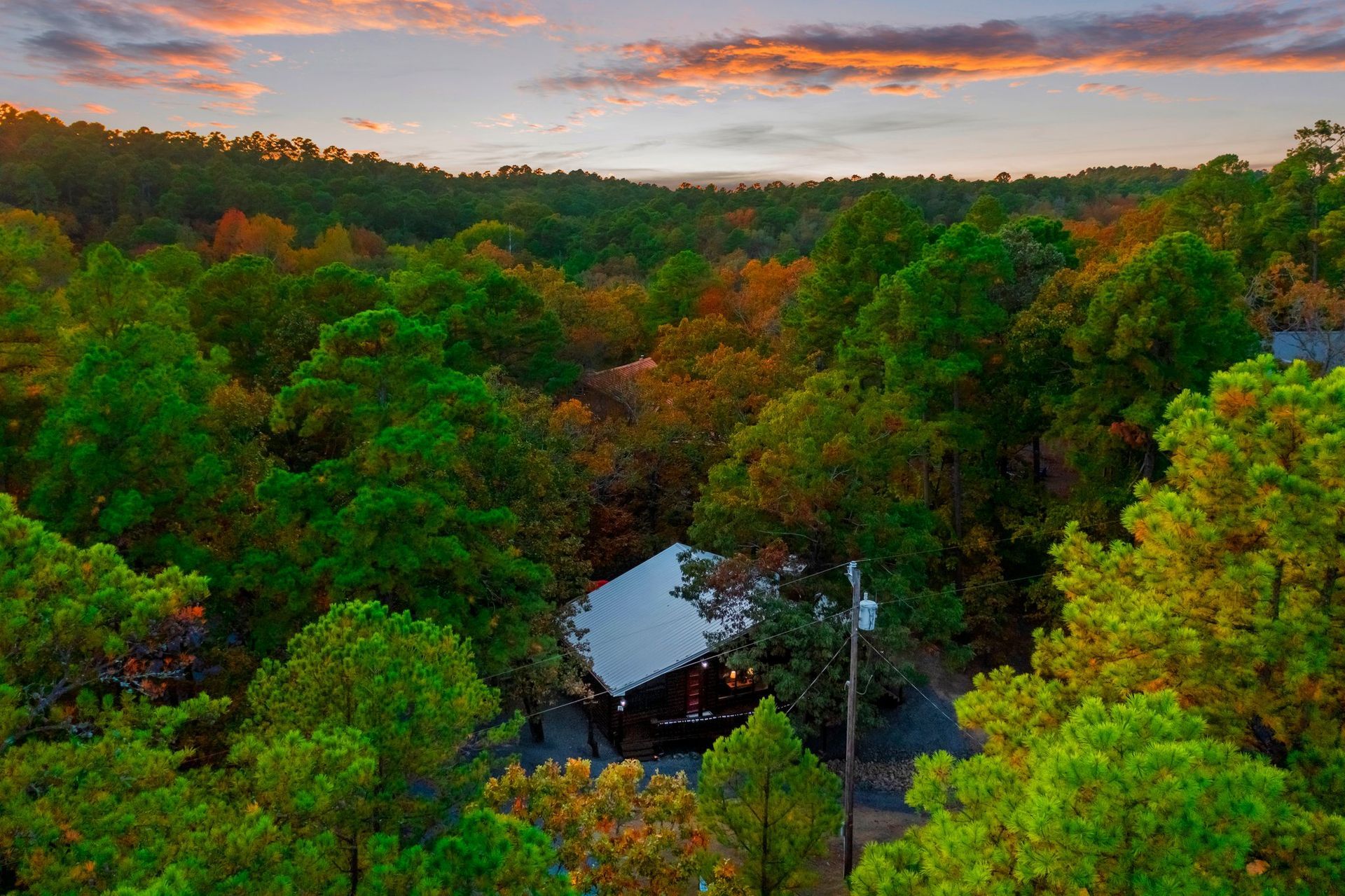 An aerial view of a house in the middle of a forest at sunset.