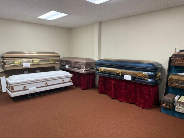 Several coffins displayed on stands in a room with beige walls and brown carpet.