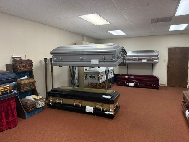 Coffins stacked in a room with shelves and storage bins, lit by overhead fluorescent lights.