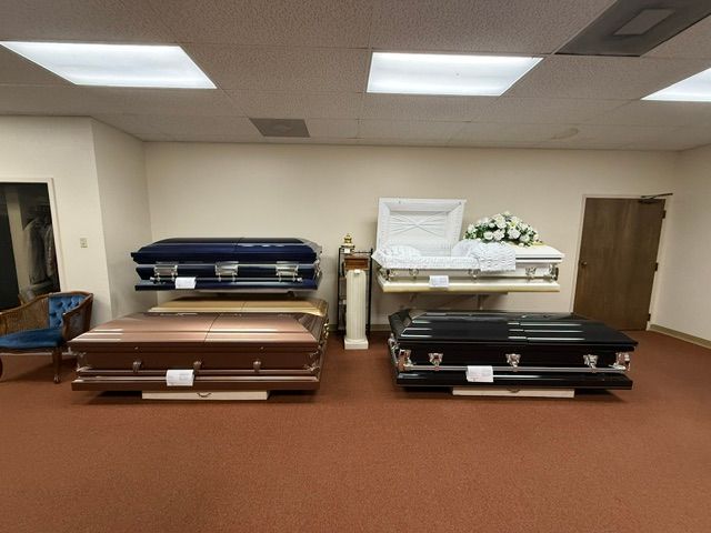 Funeral home showroom with four caskets in navy, white, brown, and black on a carpeted floor