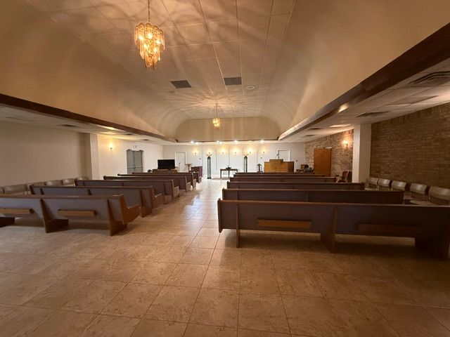 Wide church sanctuary with pews, tiled floor, vaulted ceiling, and chandelier lighting