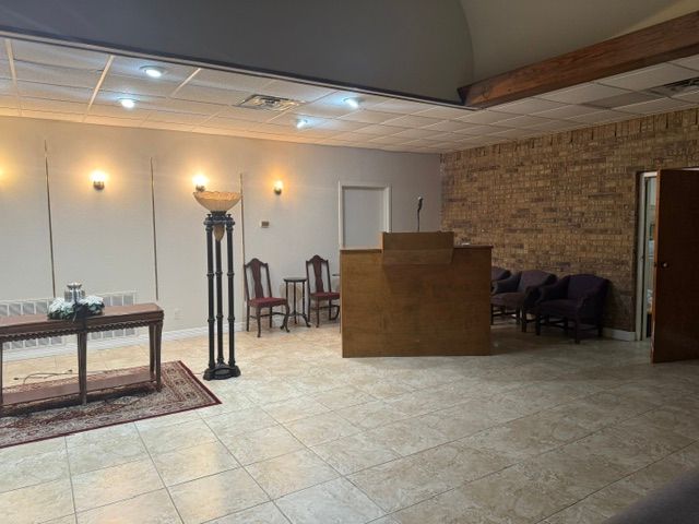 Empty lobby with tiled floor, wooden reception desk, wall sconces, and seating area against a brick wall.