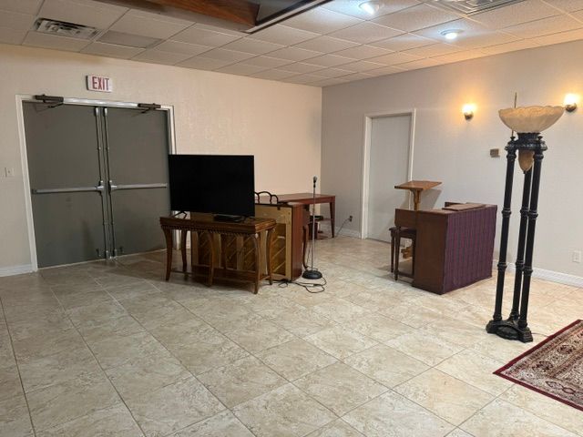 Empty hall with tiled floor, double doors, TV, podium, and tall lamp in a beige room.