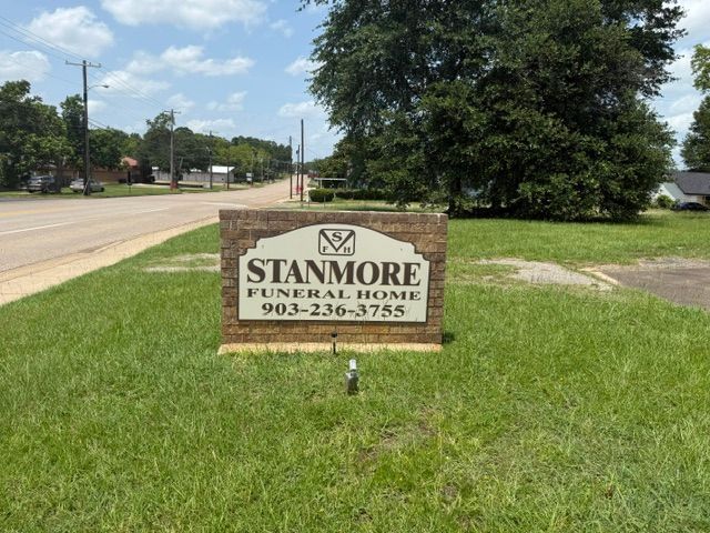 Stanmore Funeral Home sign on a grassy roadside beside a street and trees.