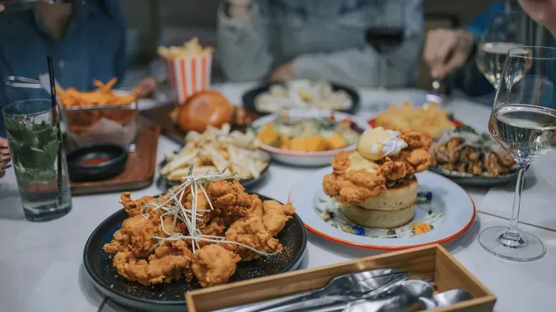 Table of fried seafood and drinks at a restaurant, with a hand reaching for food and a striped popcorn tub.
