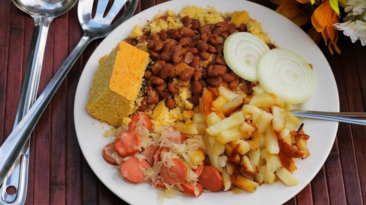 Plate of rice with beans, yams, plantains, onion slices, and cornbread on a table