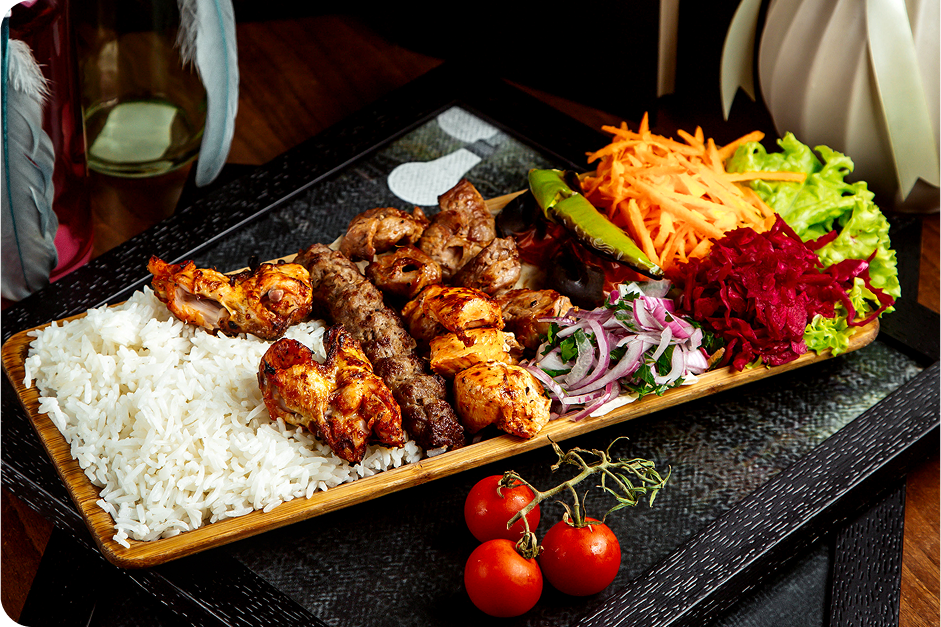 Grilled chicken platter with rice, shredded vegetables, salad, and cherry tomatoes on a table