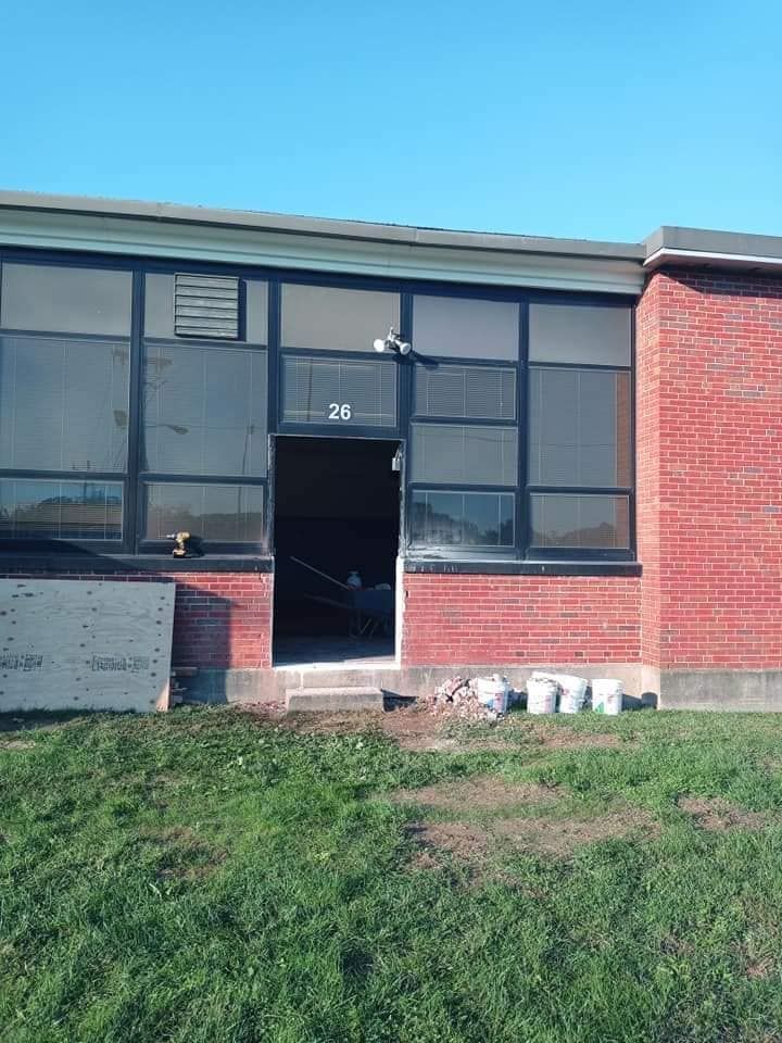 Single-story brick building entrance with dark windows and an open door under a clear blue sky.
