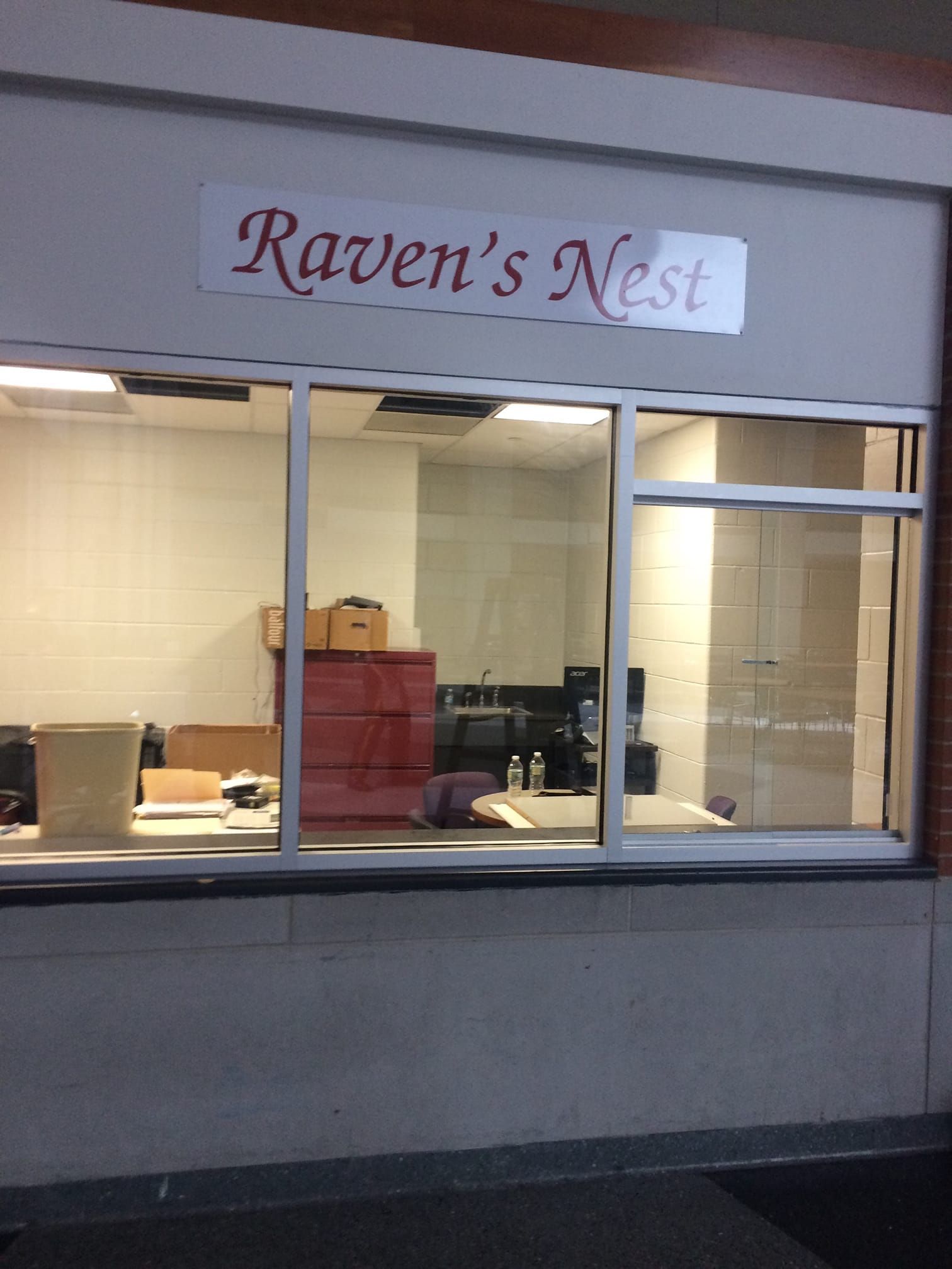 Storefront window with a “Raven’s Nest” sign above it and office furniture visible inside.