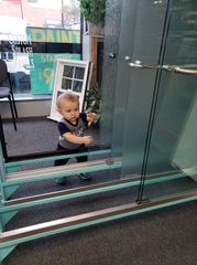 Small child standing near a glass wall, holding the frame and looking forward.