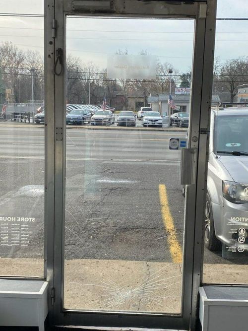 View through a glass door onto a parking lot with cars and a yellow curb line