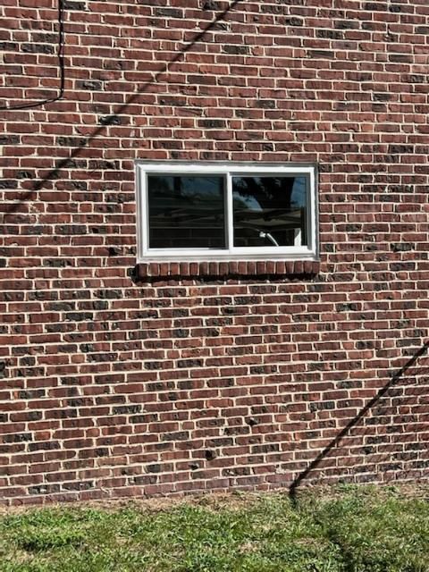 Brick exterior wall with a white-framed window and diagonal dark stains above green grass.