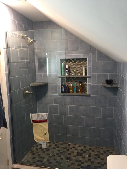 Gray-tiled bathroom shower with built-in niche shelves, glass door, and mosaic floor tile