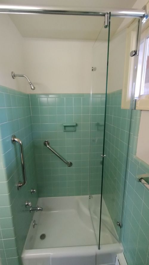 Accessible bathroom shower with grab bars, a handheld showerhead, and teal tile walls.