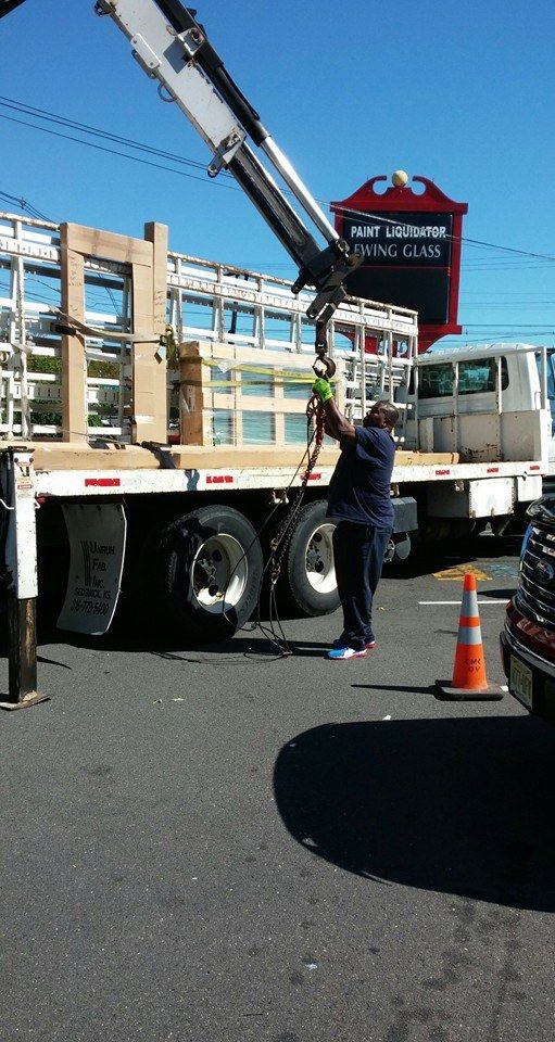 Worker standing by a crane truck lifting a red sign on a street, with orange cones nearby