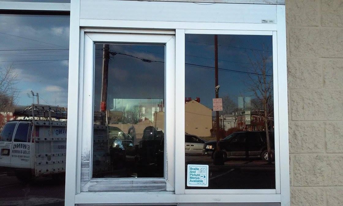 Glass storefront windows with a white frame reflecting the street and nearby buildings
