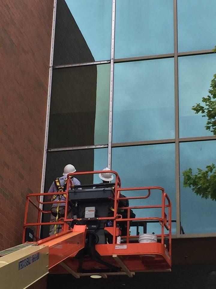 Worker on an orange cherry picker cleaning or inspecting a glass building facade